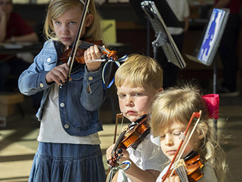 three young children playing violin